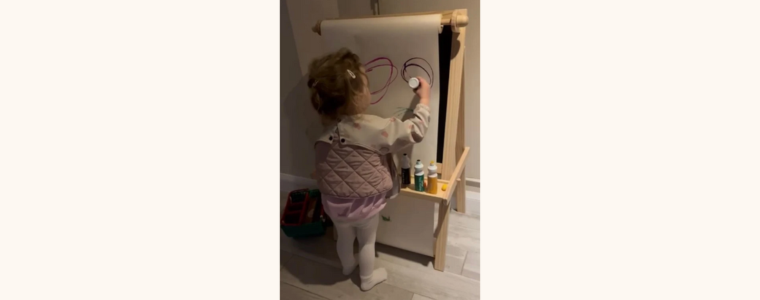 "A little girl painting on a vertical easel."