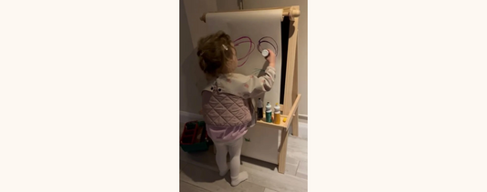 "A little girl painting on a vertical easel."