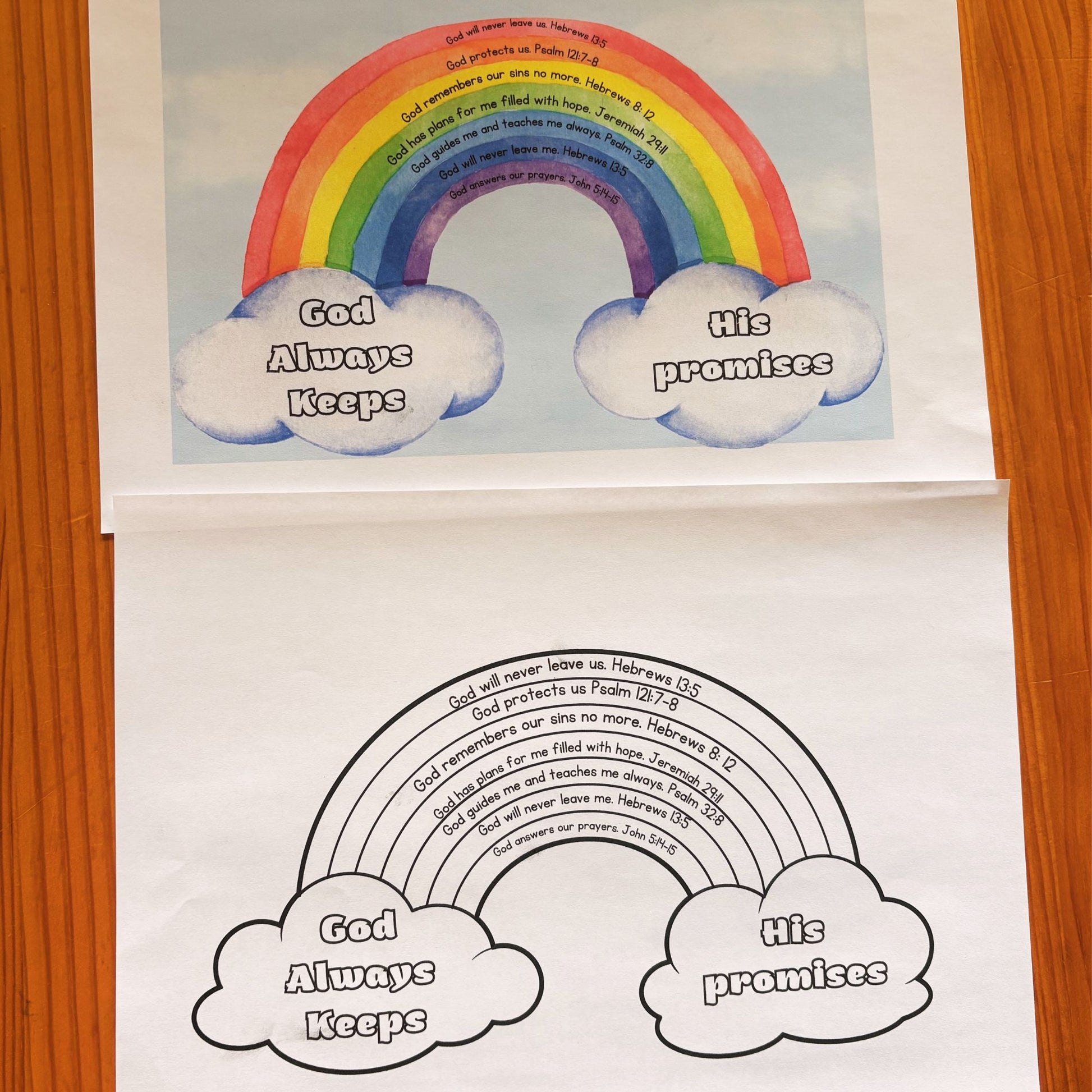 A printed rainbow-themed scripture poster and colouring page laid on a wooden surface, showing a colourful rainbow with clouds reading 'God Always Keeps' and 'His promises,' plus a black-and-white version. 