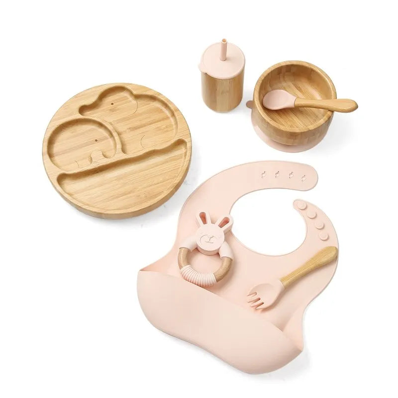 "A pink and bamboo bib, rattle, beaker, spoon, fork, bowl, plate for babies and toddlers."