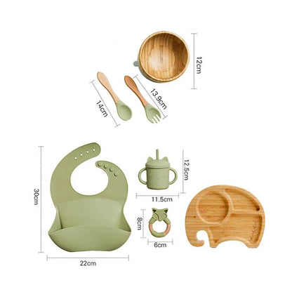 "A green and bamboo bib, rattle, cup, spoon, fork, bowl, elephant shaped plate for babies and toddlers ."