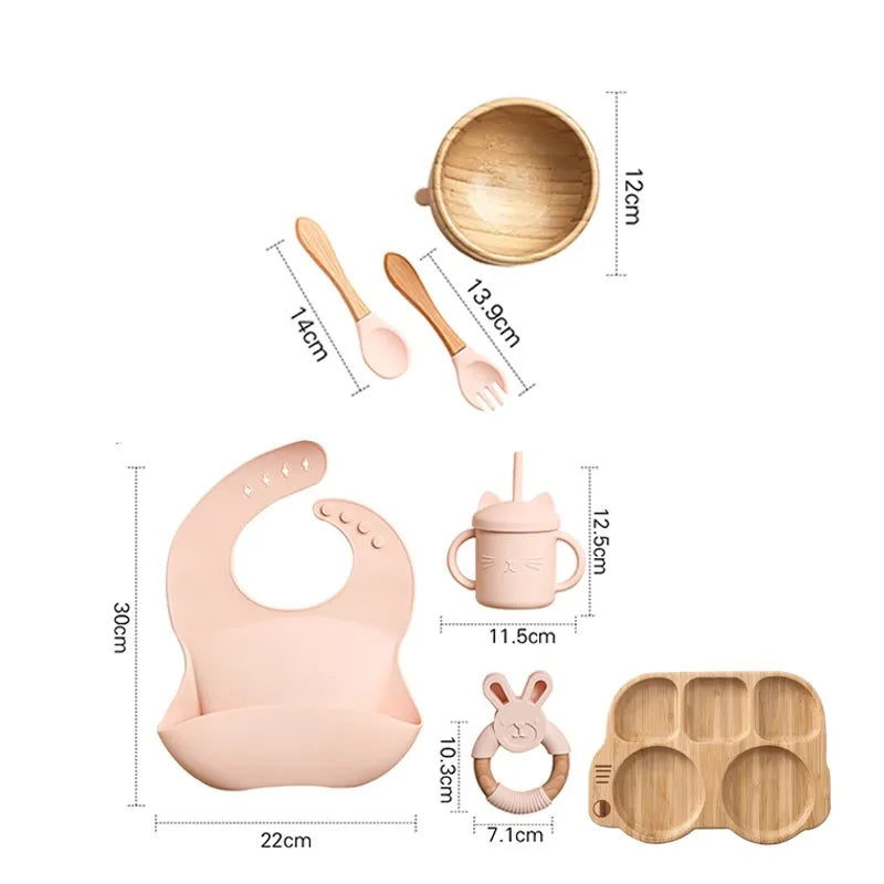 "A pink and bamboo bib, rattle, cup, spoon, fork, bowl, bus shaped plate for babies and toddlers ."