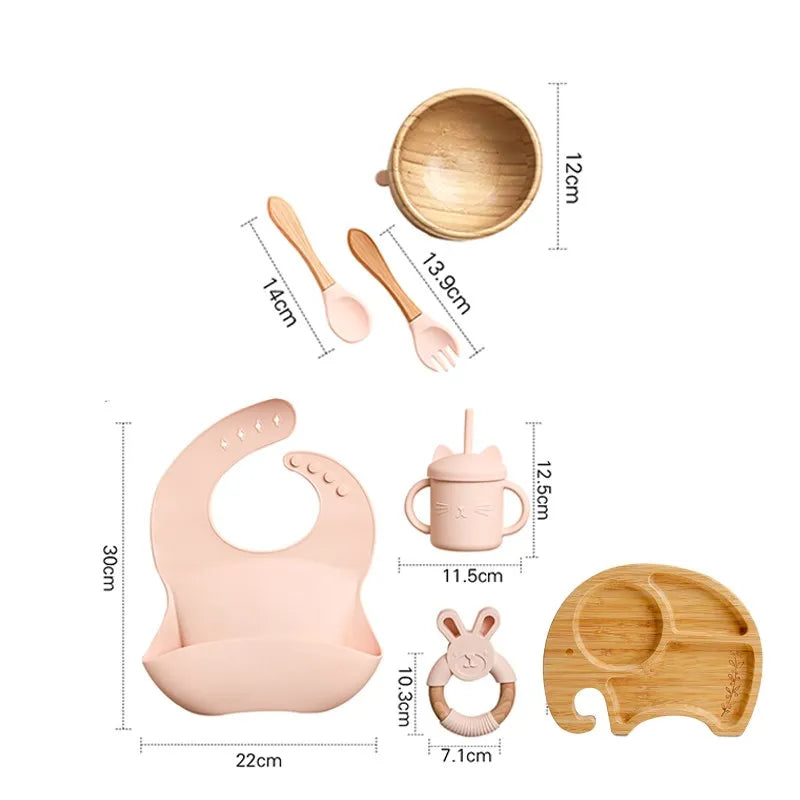 "A pink and bamboo bib, rattle, cup, spoon, fork, bowl, elephant shaped plate for babies and toddlers."