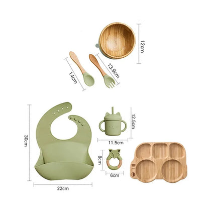 "A green and bamboo bib, rattle, cup, spoon, fork, bowl, bus shaped plate for babies and toddlers ."