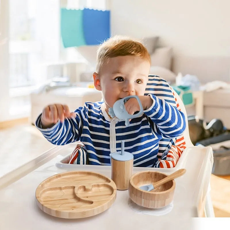 "A toddler sat in a highchair with a bamboo dinner set "