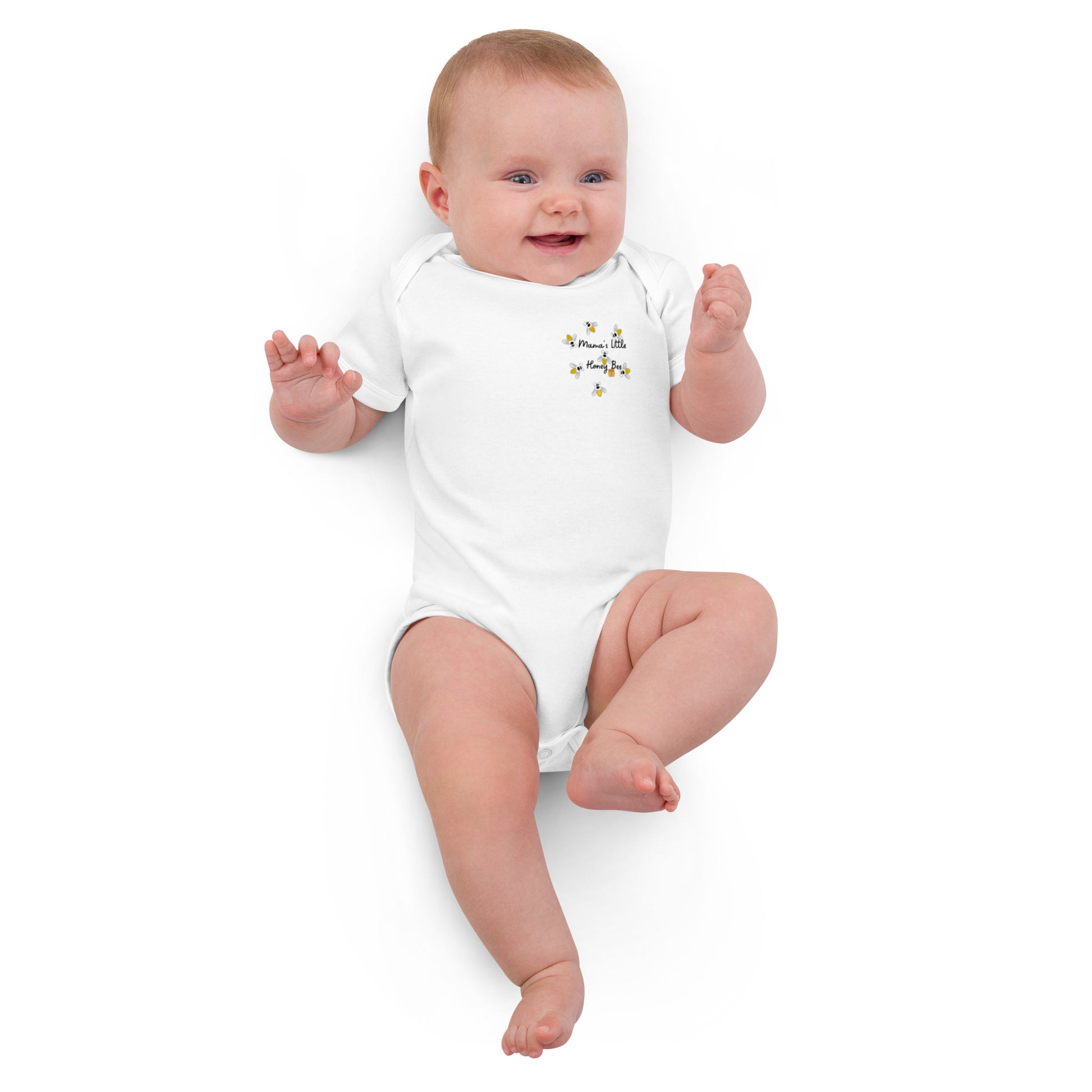 "A baby lying down smiling wearing a mama's little honey bee white bodysuit."