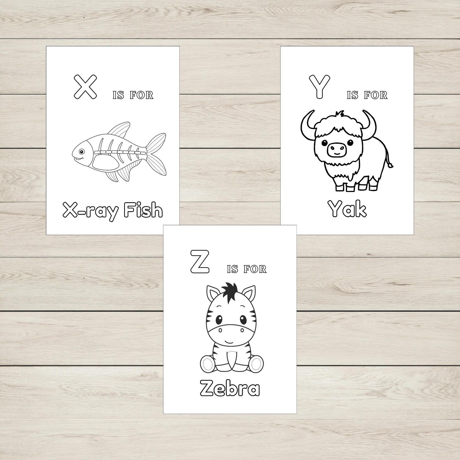 Three colouring sheets with animal illustrations and letters on a wooden surface.